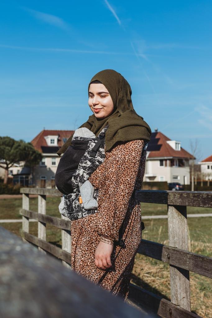 Feride staat glimlachend bij een houten hek, met een blauwe lucht erachter