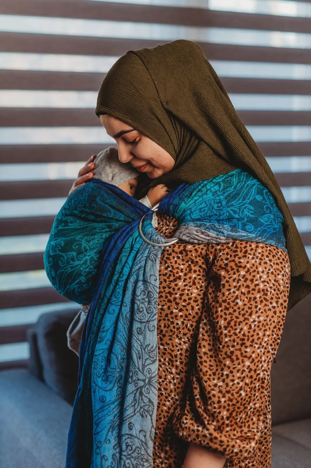 Feride draagt haar baby binnenshuis in een blauwe geweven ringsling